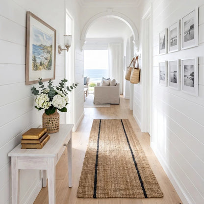 Hallway with a woven rug, white bench, and framed pictures on a white wall.