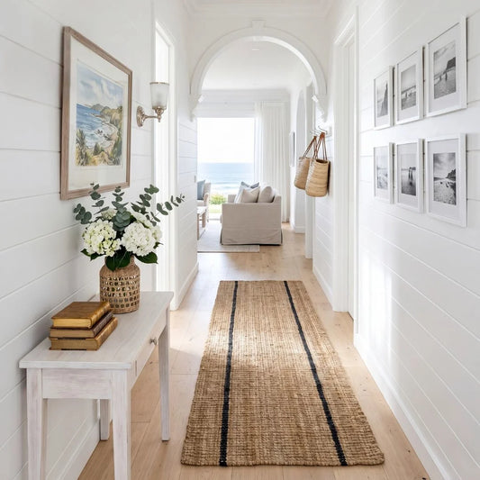 Hallway with a woven rug, white bench, and framed pictures on a white wall.