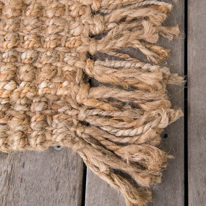 Close-up of a textured woven jute mat with fringes on a wooden surface