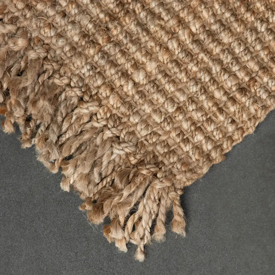Close-up of a textured jute rug corner on a gray background