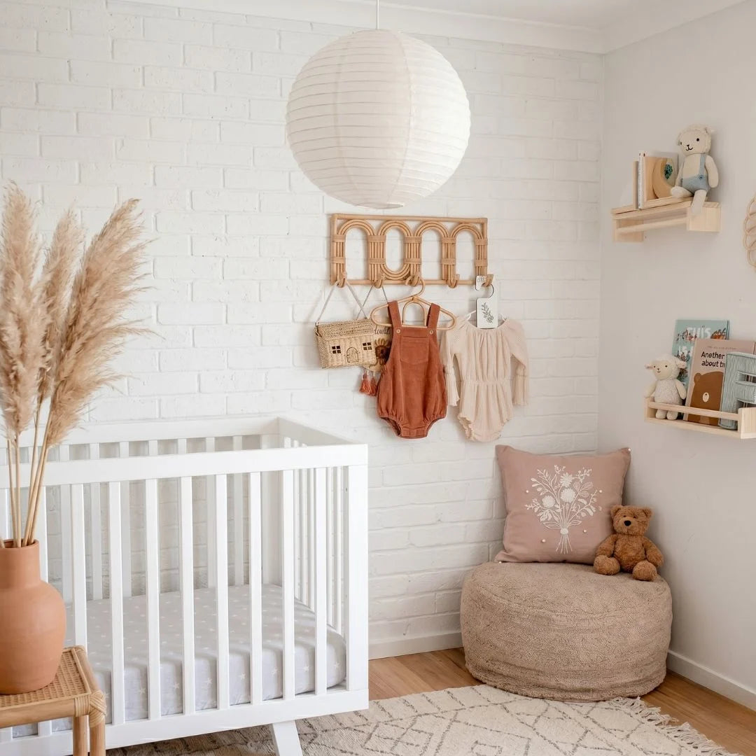 Nursery room with white crib, beige ottoman, round white linen pendant and decorative items.