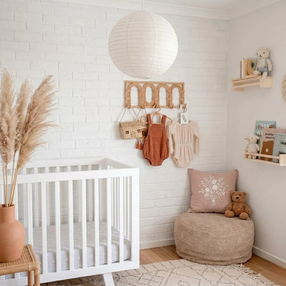 Nursery room with white crib, beige ottoman, round white linen pendant and decorative items.