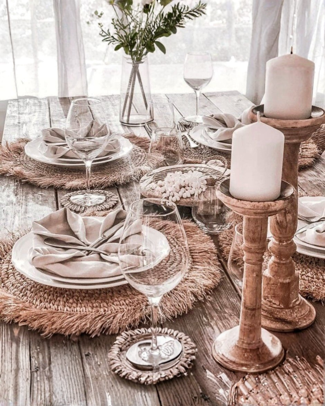 Elegant table setting with candles, glasses, and plates on a wooden table.
