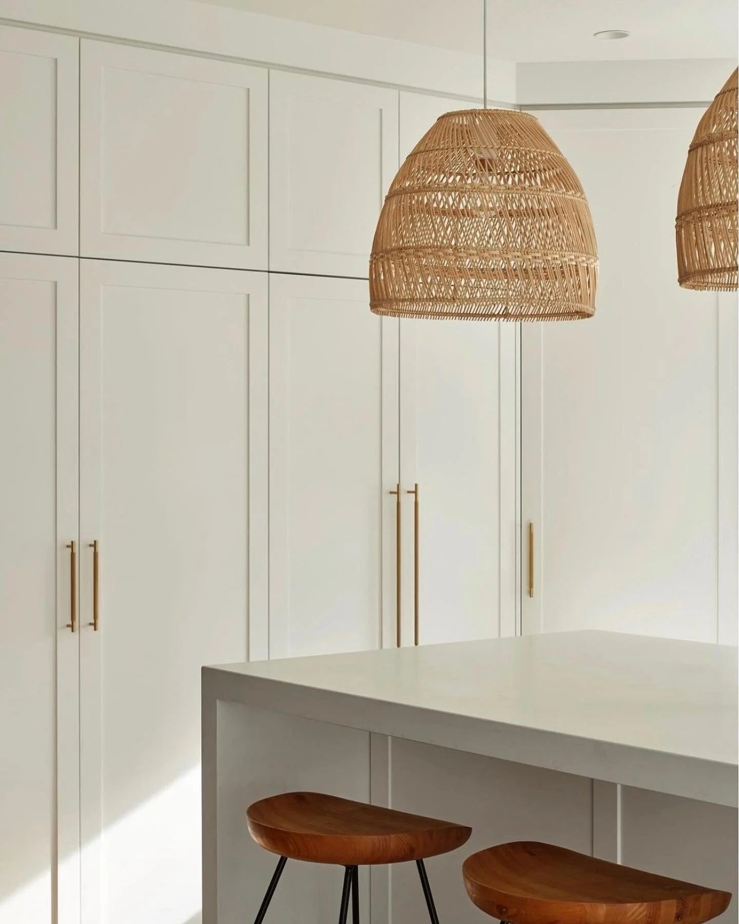 Modern kitchen with white cabinetry, rattan pendant lights, and wooden stools.
