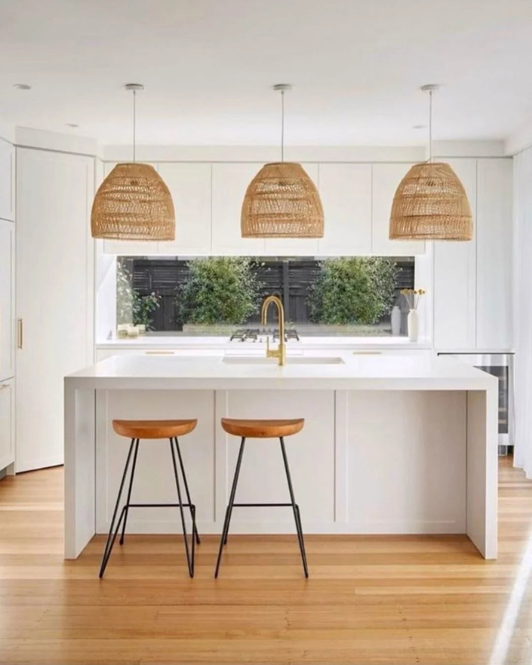 Modern kitchen with white island, wooden stools, and wicker pendant lights.