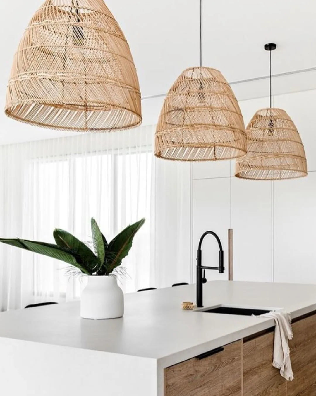 Modern kitchen with wicker pendant lights, white countertops, and a plant.