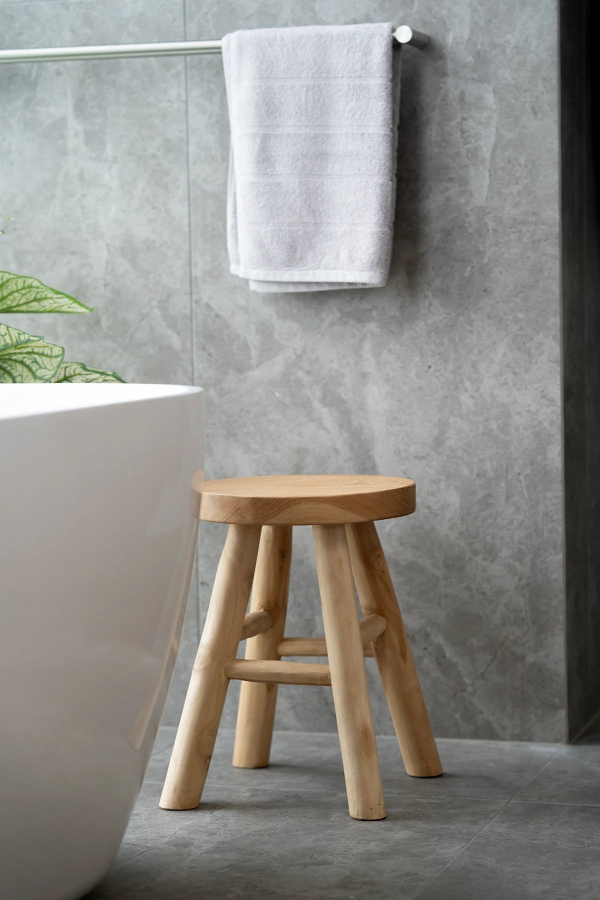 Wooden stool in a bathroom with a gray tiled wall and white bathtub.