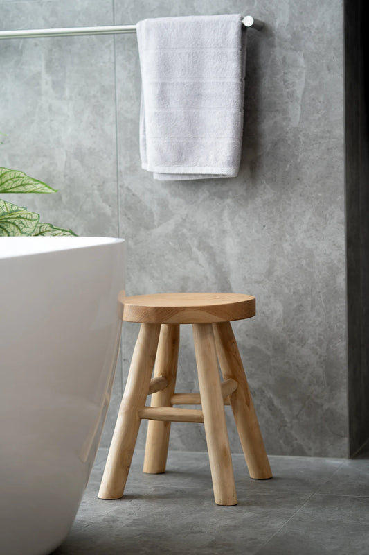 Wooden stool in a bathroom with a gray tiled wall and white bathtub.