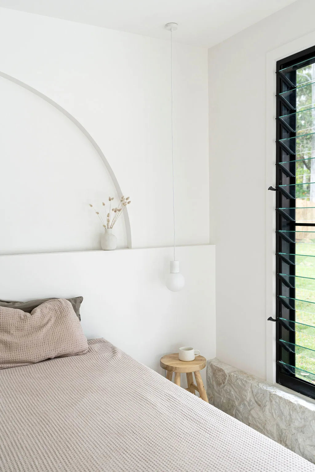 Modern bedroom with a bed, side table, and window with black frame.