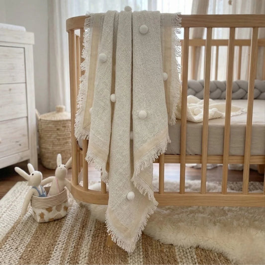 Wooden crib with a textured white blanket draped over it in a nursery setting.