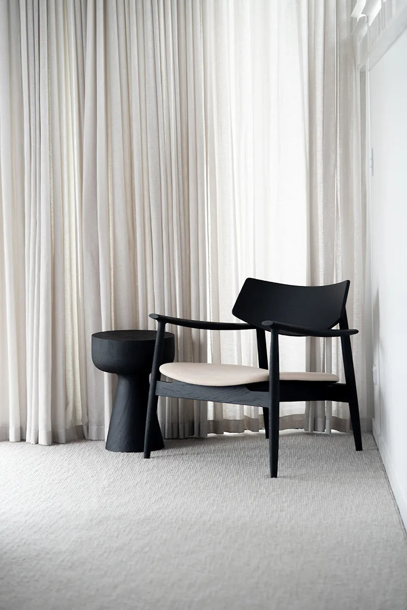Black armchair and the Olli oak black stump side table in a room with white curtains and carpet.