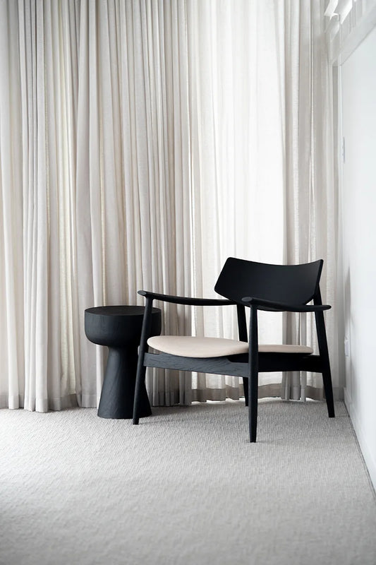 Black armchair and the Olli oak black stump side table in a room with white curtains and carpet.