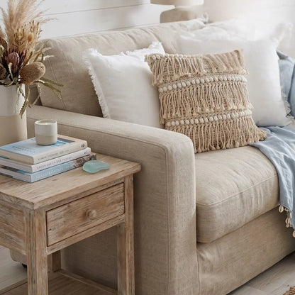 Beige sofa with decorative pillows and a wooden side table with books and a candle.