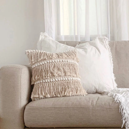 Beige sofa with textured pillow and white blanket in a room with light filtering through sheer curtains.