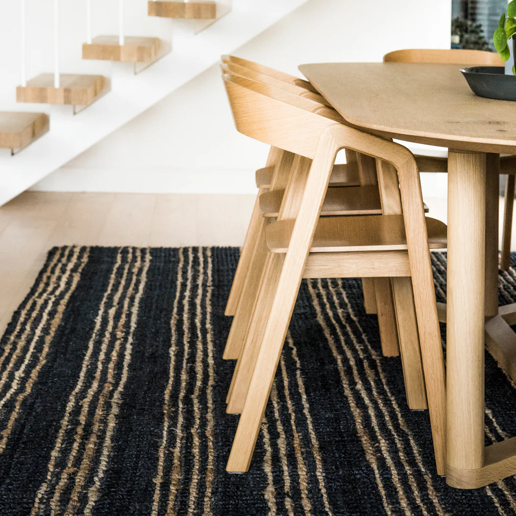 Wooden dining table and chairs on a black and gold striped rug with a white wall and staircase in the background.