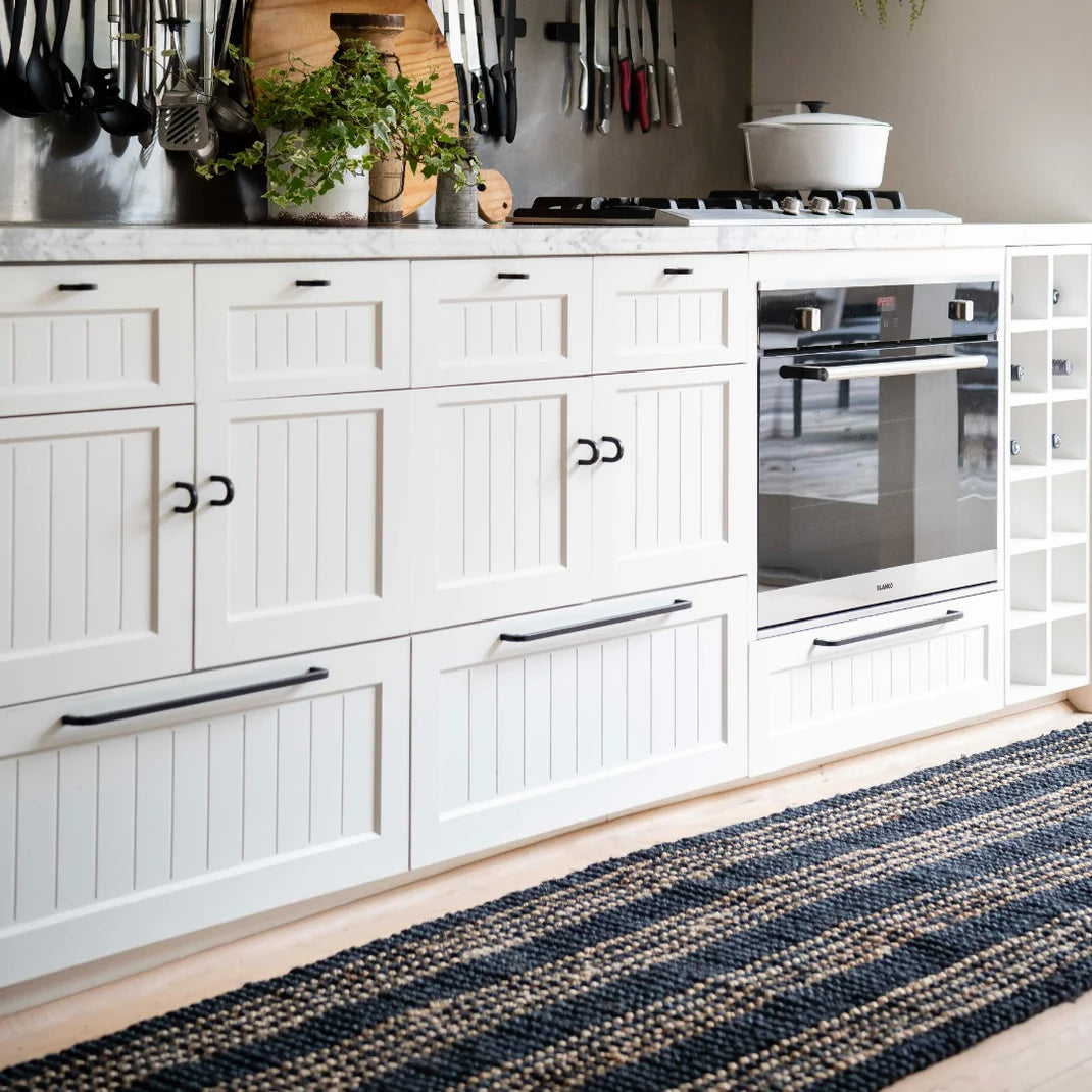 Modern kitchen with white cabinets, black handles, and a striped rug on the floor.