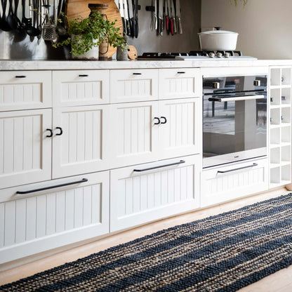 Modern kitchen with white cabinets, black handles, and a striped rug on the floor.