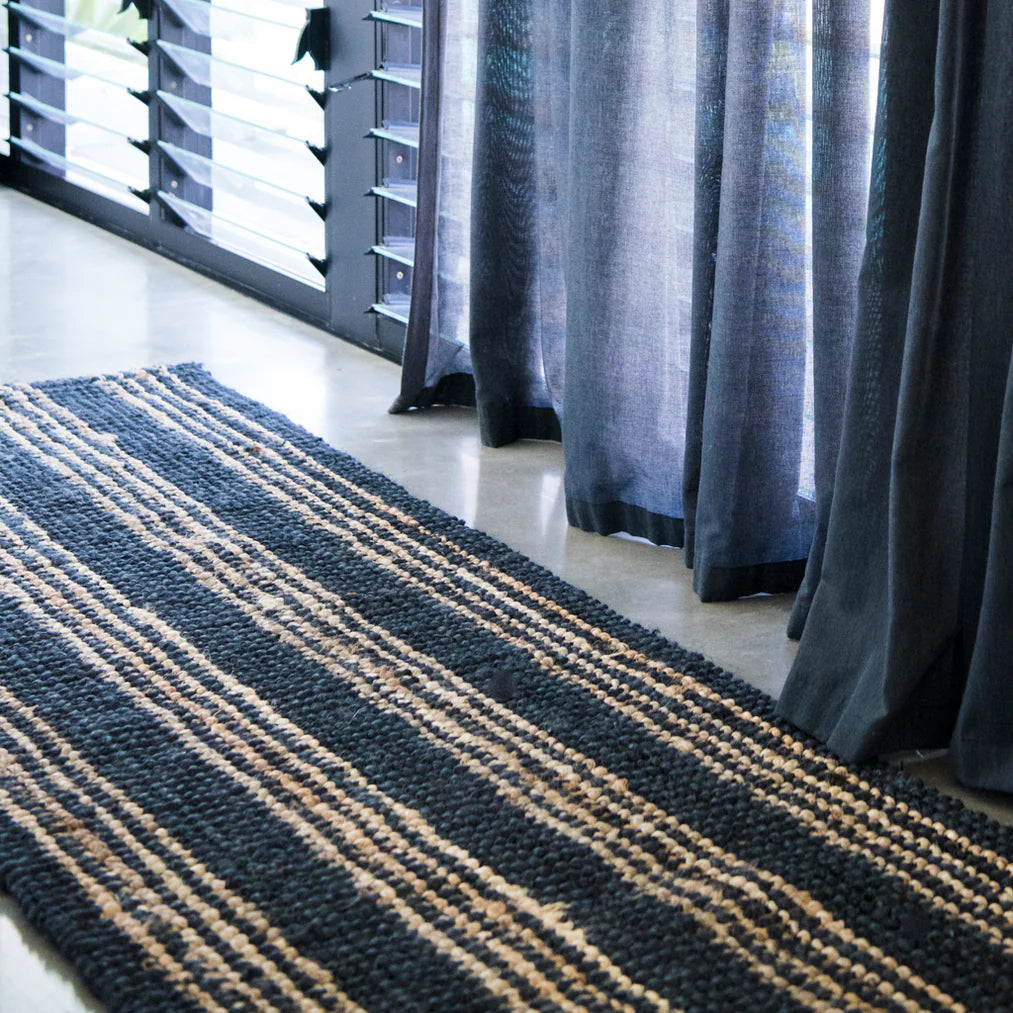 Textured black and beige rug on a light wood floor with gray curtains.