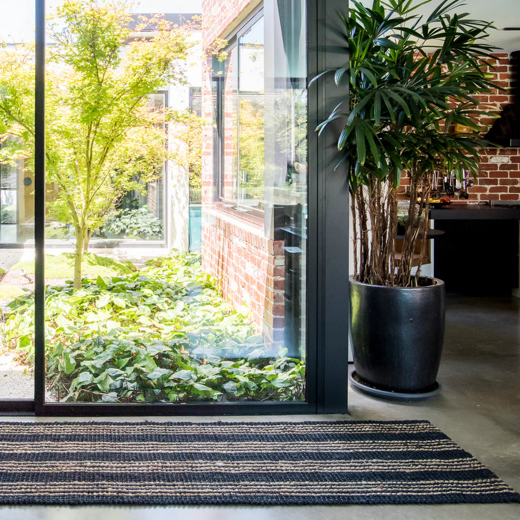 Modern interior with a large glass door leading to a garden, featuring a potted plant and striped rug.