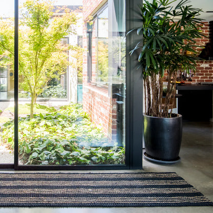 Modern interior with a large glass door leading to a garden, featuring a potted plant and striped rug.