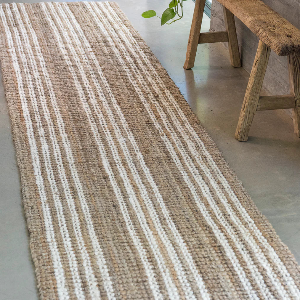 Striped jute rug on a concrete floor with a wooden bench in the background.