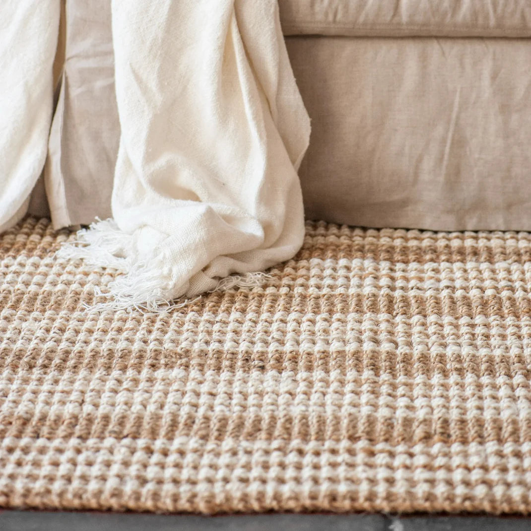 Textured beige rug with a draped white fabric on a neutral background