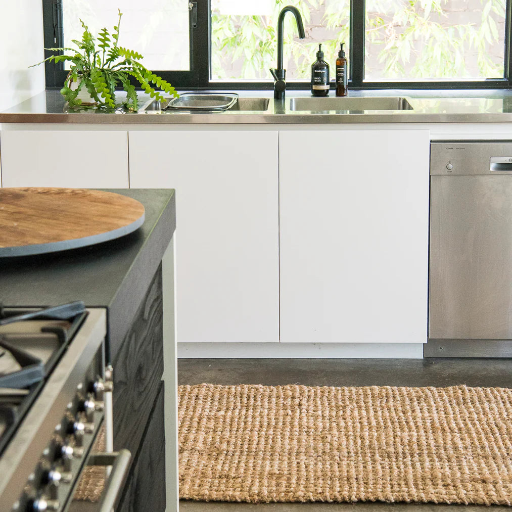 Modern kitchen with white cabinets, stainless steel appliances, and a woven mat on the floor.