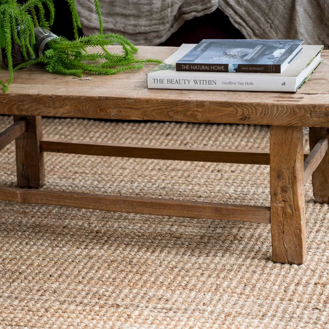 Wooden coffee table with books and a plant on a textured rug