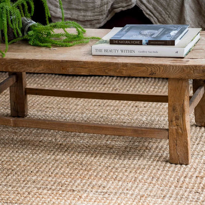 Wooden coffee table with books and a plant on a textured rug