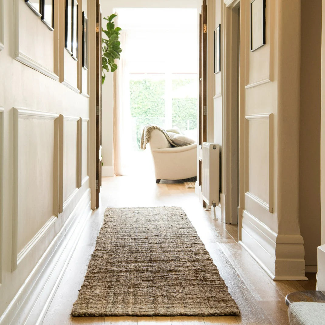 Hallway with a textured jute rug leading to a living room with a white armchair.