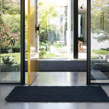 Modern interior with large glass doors and black doormats on a light wood floor.