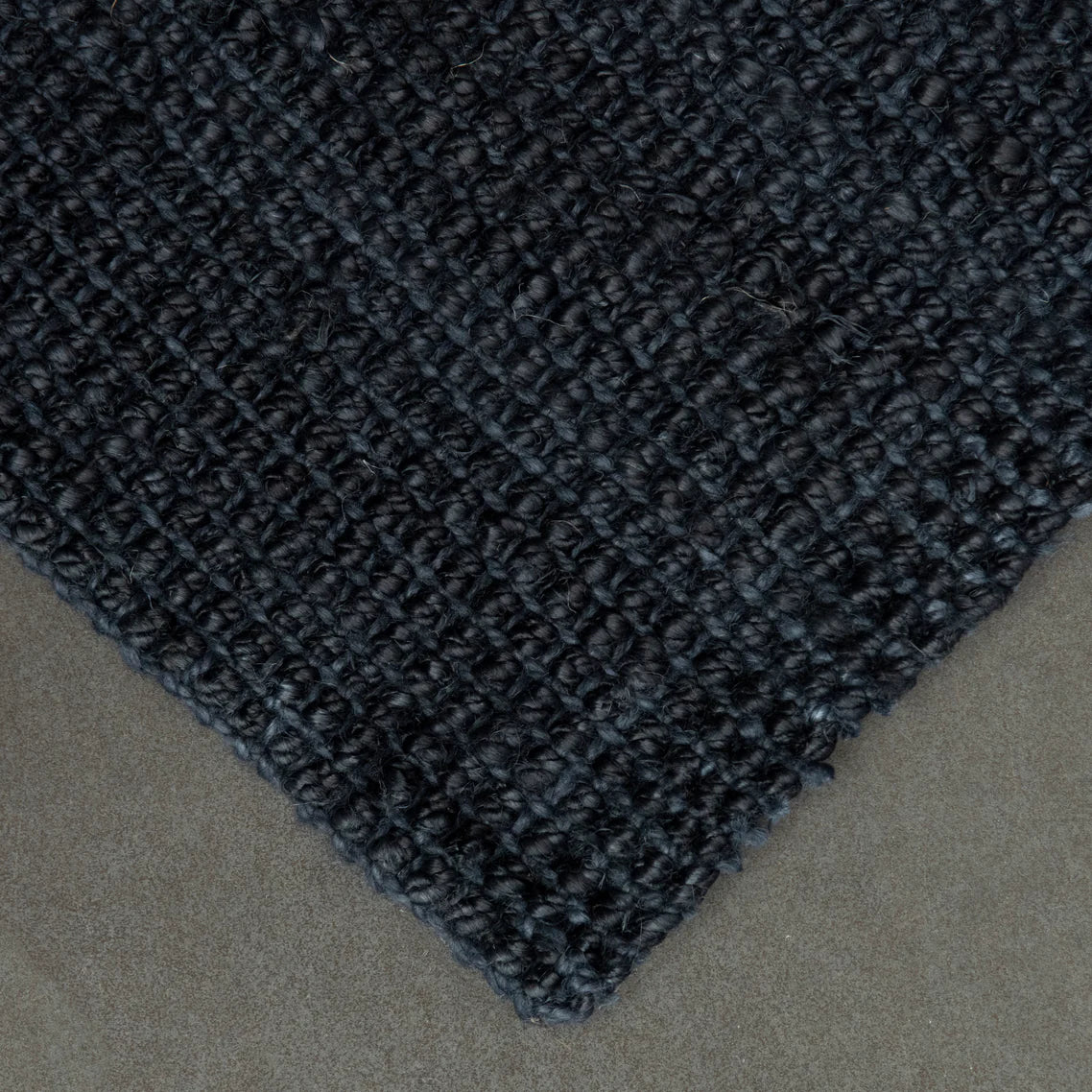 Close-up of a textured black rug corner on a neutral background