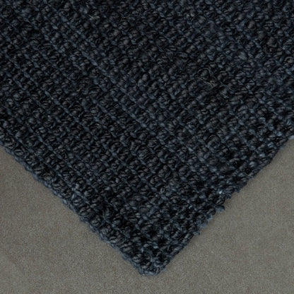 Close-up of a textured black rug corner on a neutral background