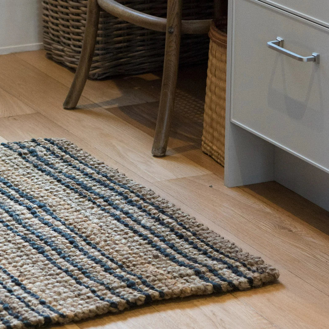 Textured rug with black and beige stripes on a wooden floor next to a wicker basket and white cabinet.