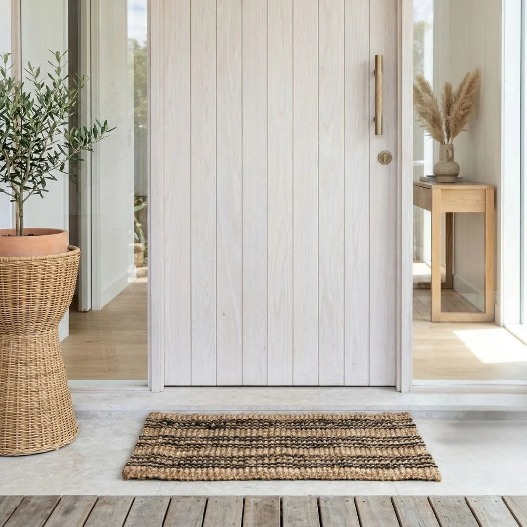 Wooden door with a woven mat on a wooden deck, featuring a plant and a small table.