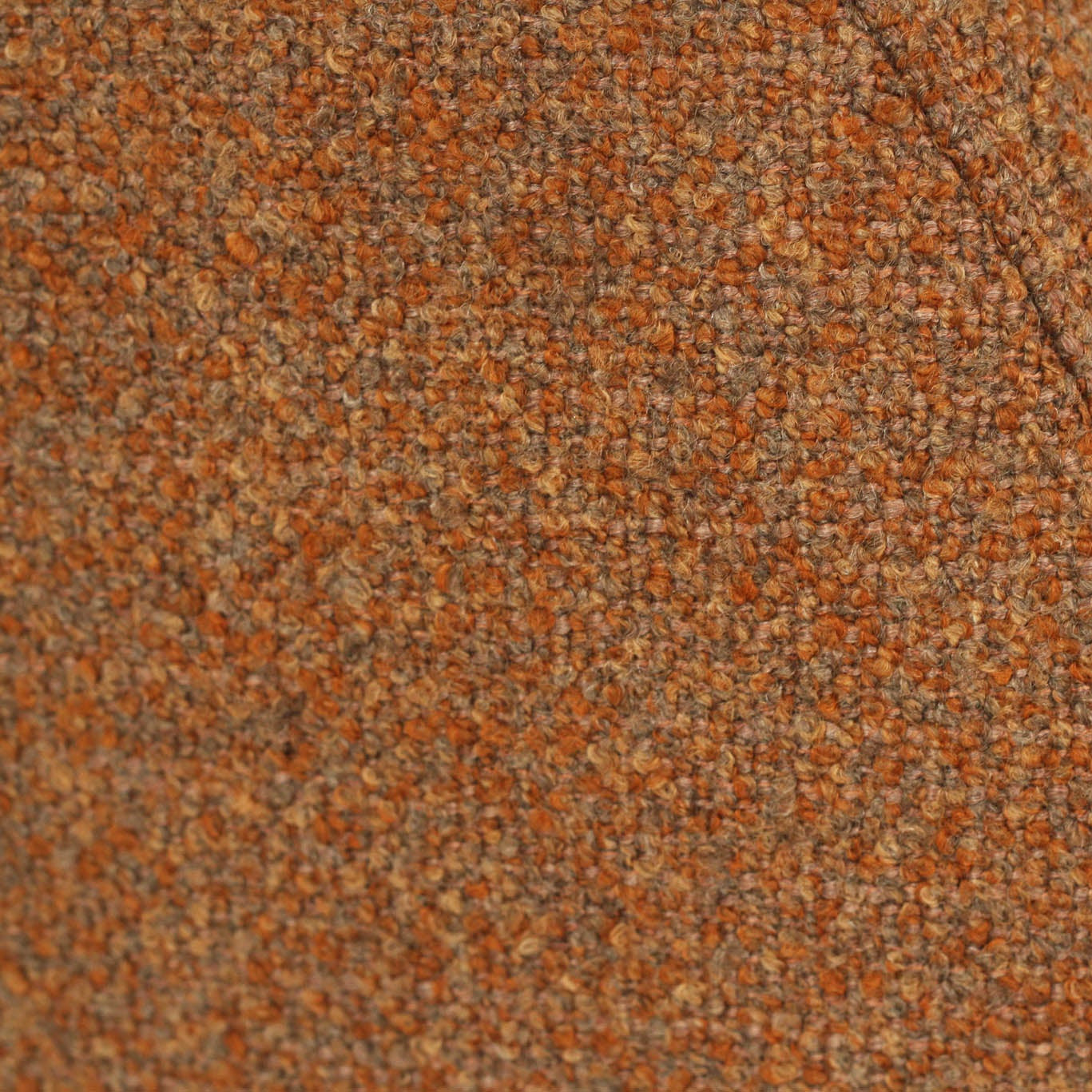 Close-up of a textured tweed fabric in a mottled blend of rust orange, brown, and beige threads, showing a curved seam against a white background.