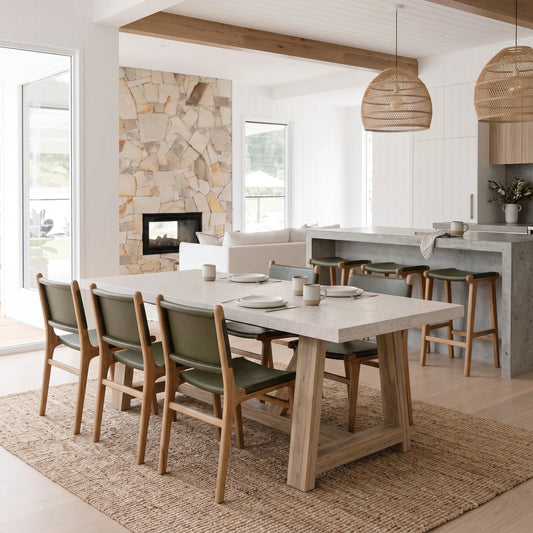 A modern dining room scene featuring a rectangular light wood and stone dining table surrounded by six mid-century style chairs with green upholstered seats, set on a woven jute rug in a bright, contemporary home.