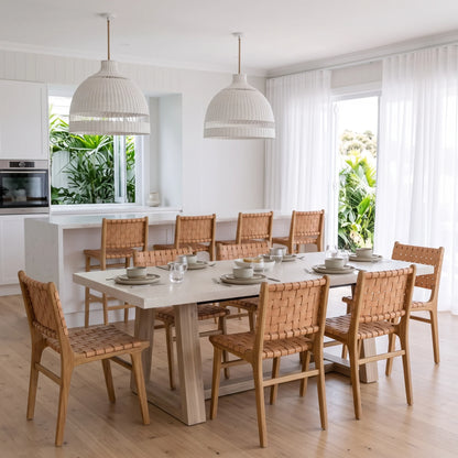 A dining room set featuring a light wood rectangular table and eight woven rattan chairs, styled with white tableware in a bright, modern kitchen-dining space.