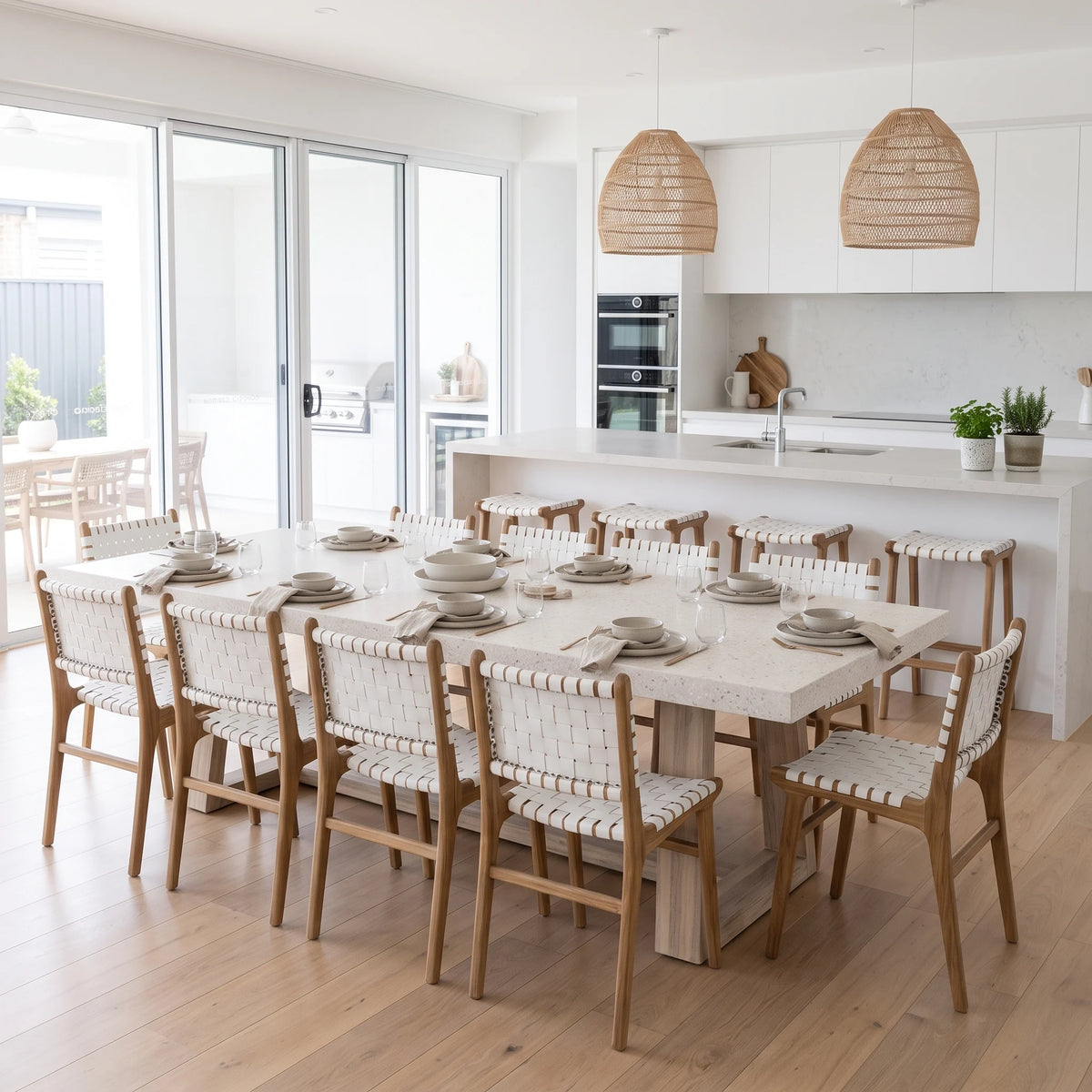 Modern kitchen and dining room featuring Sun Republic Otis woven leather and teak dining chairs and stools, rattan pendants and terrazzo stone dining table