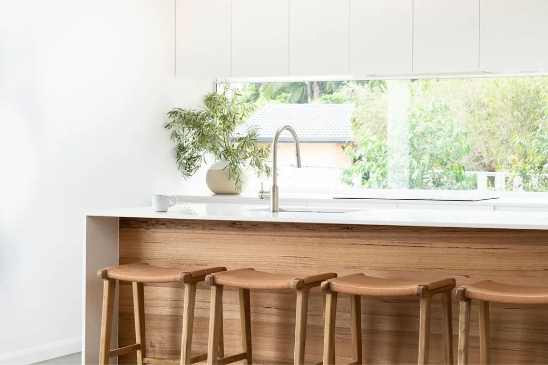 Natural Tan Leather and Teak stools in front of a kitchen counter with a window view.