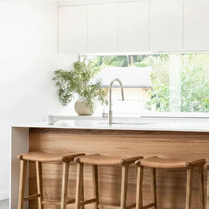 Natural Tan Leather and Teak stools in front of a kitchen counter with a window view.