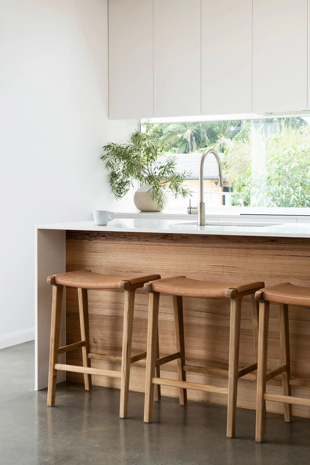 Natural Tan Leather and Teak stools in front of a kitchen counter with a window view.