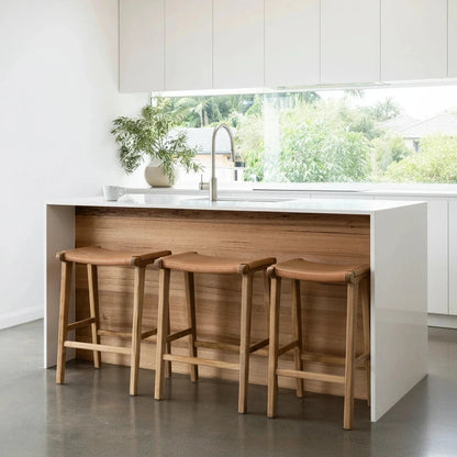 Natural Tan Leather and Teak stools in front of a kitchen counter with a window view.