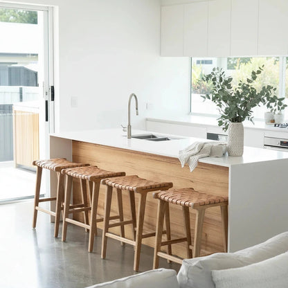 Wooden bar stools in a modern kitchen setting with white cabinets and a sink.