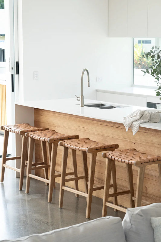 Wooden bar stools in a modern kitchen setting with white cabinets and a sink.