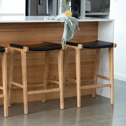 close up of otis black leather and teak kitchen stools in a kitchen setting.