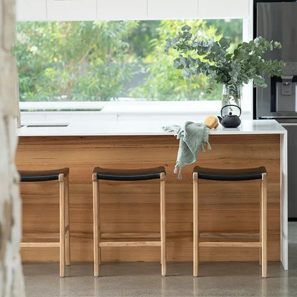 Modern kitchen with wooden bar stools and a window view of garden.