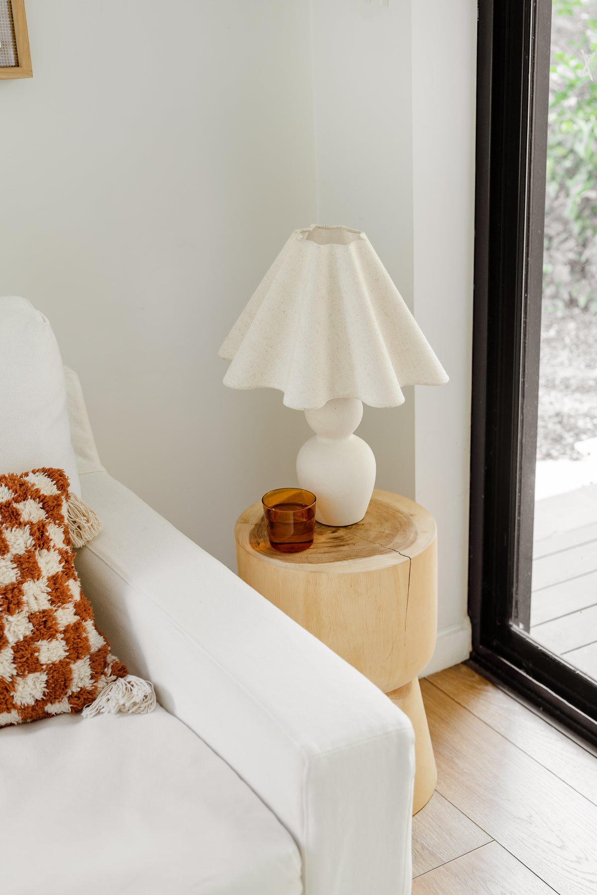 White lamp on a wooden side table next to a white sofa with a patterned pillow.
