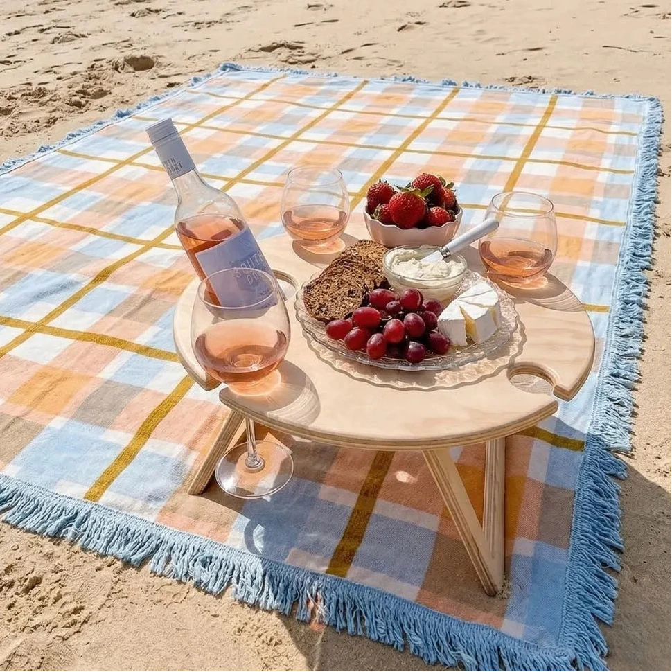 Picnic setup on a beach with a checkered blanket, table, wine, and food.