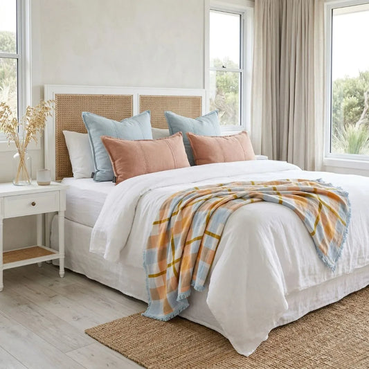 Bedroom with a neatly made bed featuring a plaid blanket and pillows, with a side table and curtains.